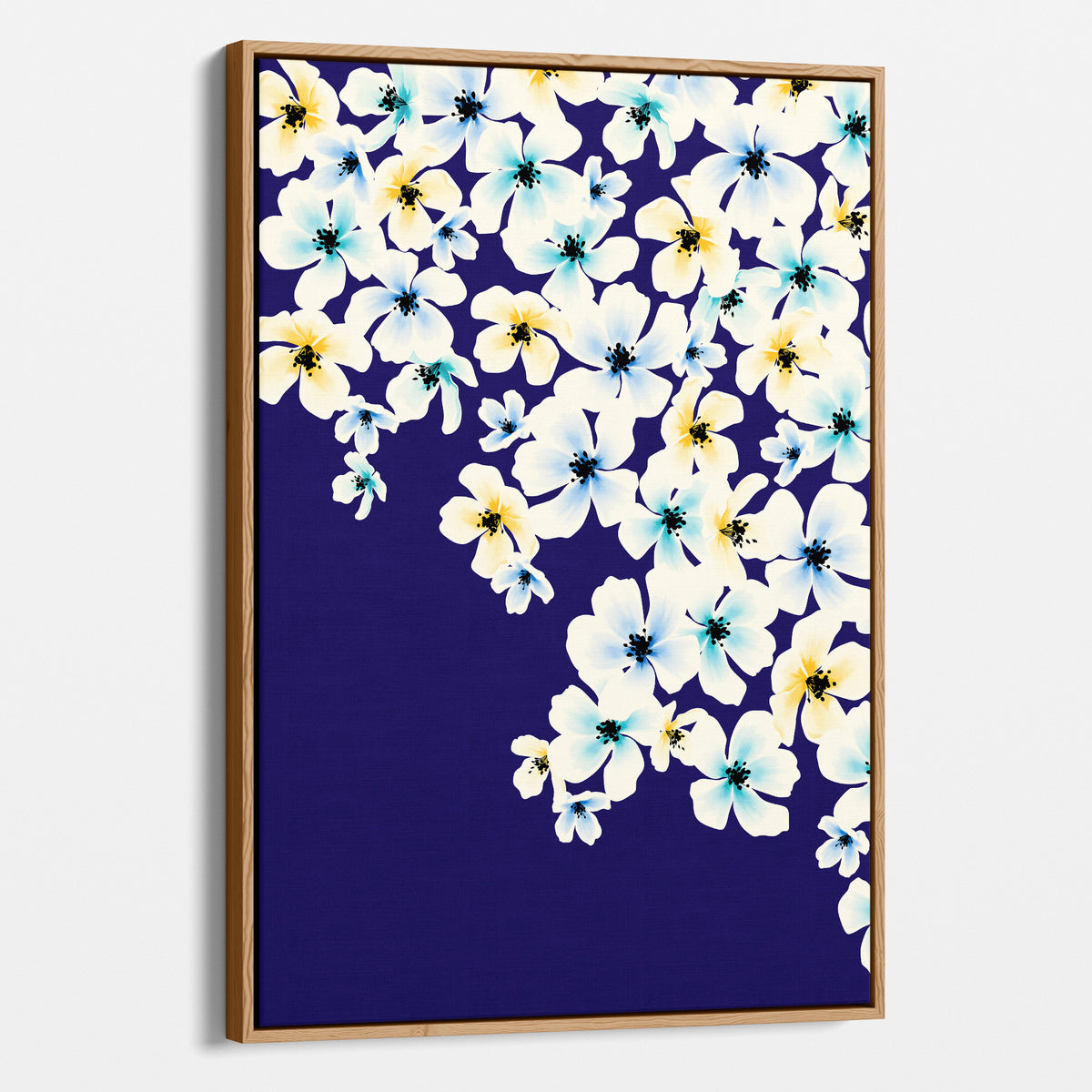 Blossom Yellow a framed wall art featuring a floral print with white, light blue, and yellow flowers on a deep navy background, shown in a light oak wood frame against a light grey wall.
