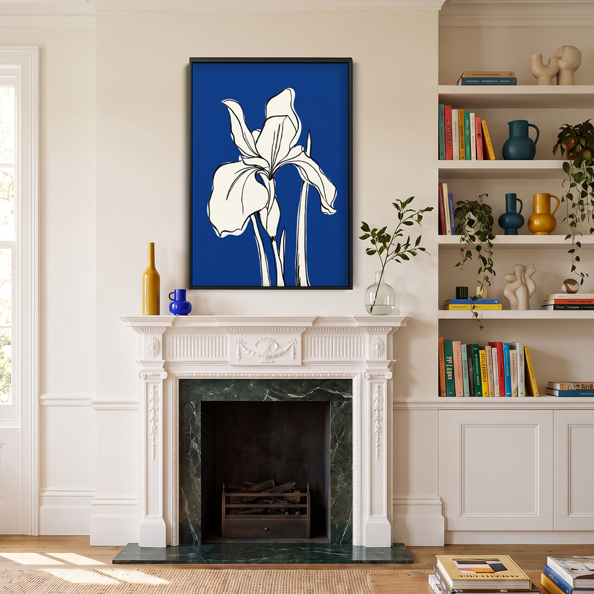 A Iris Blue framed wall art print featuring a white iris flower on a vivid blue background, displayed above a white fireplace mantel in a styled living room with shelves, books, and decorative vases.