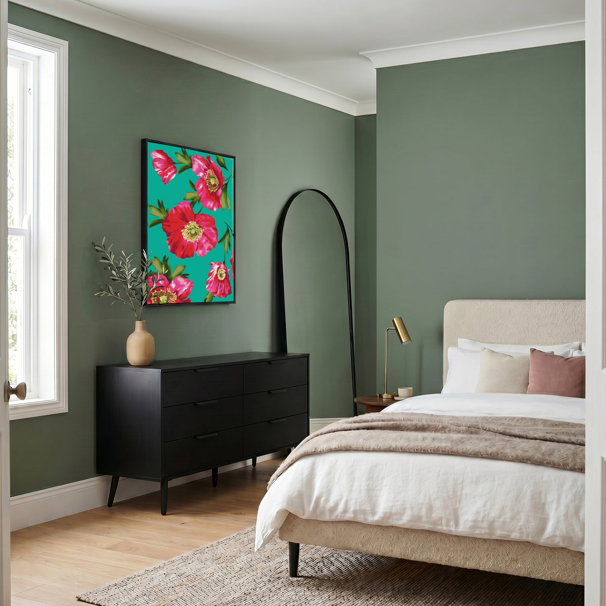A styled bedroom interior with sage green walls, a beige upholstered bed, white bedding, a black dresser, and a colourful Isla Turquoise floral wall art piece above it.
