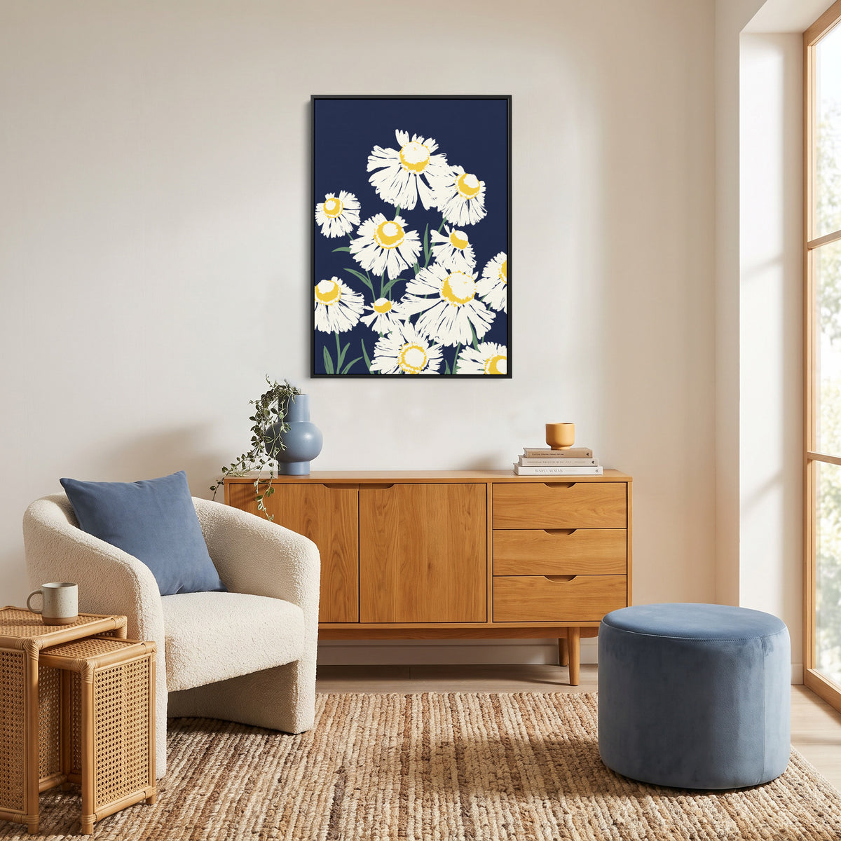 Margarite Navy  art print featuring white daisies with yellow centers on a dark navy background, displayed above a light wood sideboard in a bright, modern living room with a cream chair, woven rug, and blue ottoman.