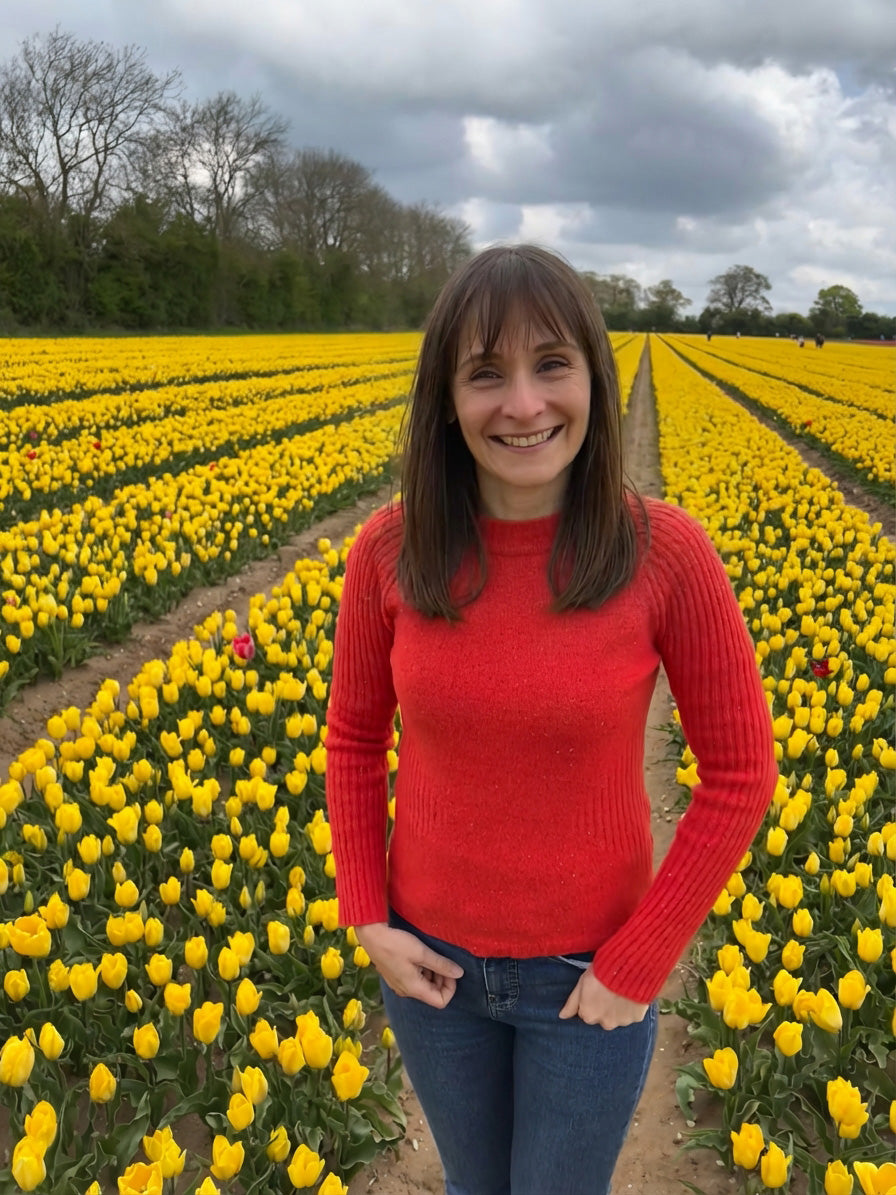 Woman in a red sweater standing in a field of yellow tulips with a cloudy sky.