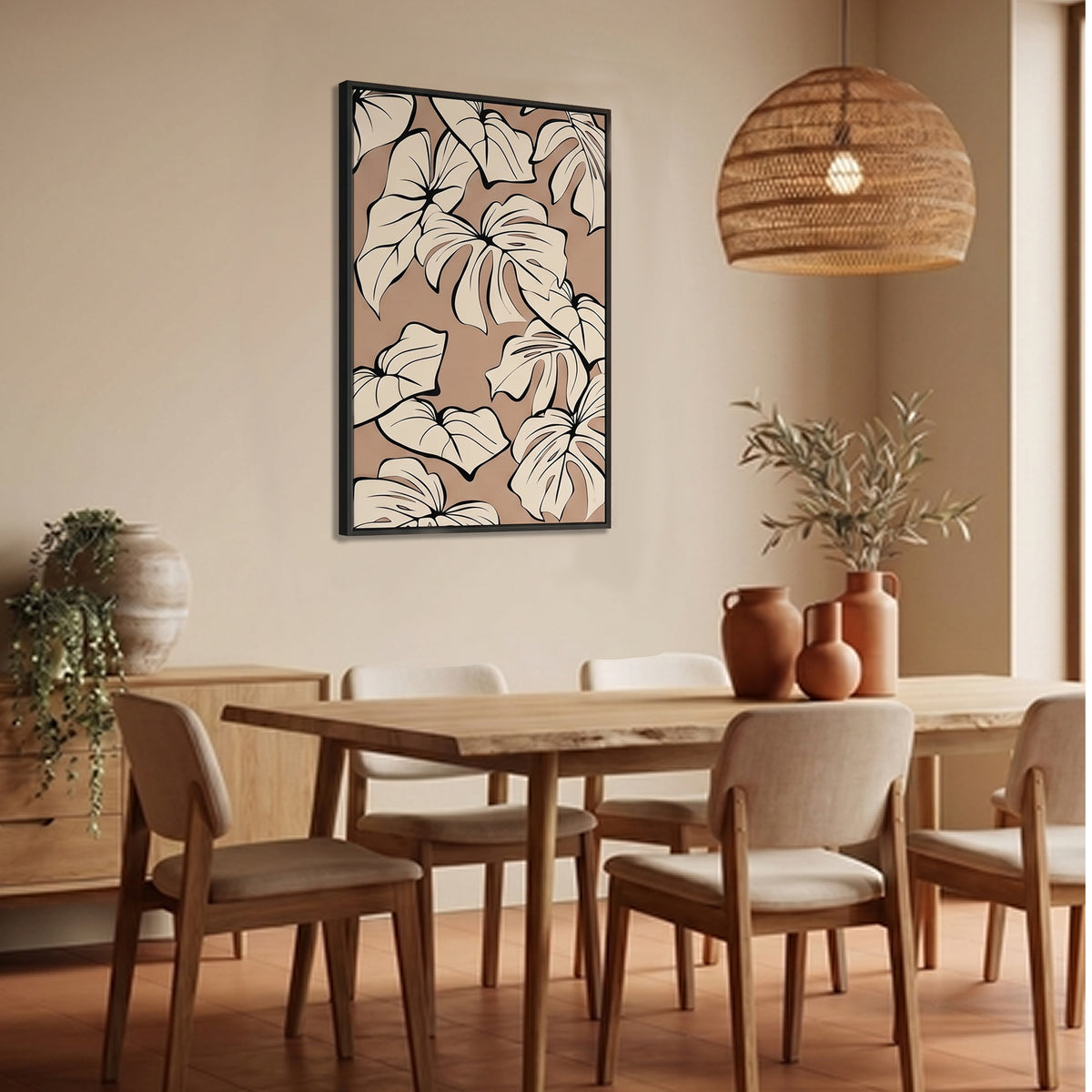 Kai Coffee framed botanical wall art print with large cream monstera leaves on a warm beige background, hanging above a wooden dining table in a styled dining room with chairs, a woven pendant light, and terracotta vases.
