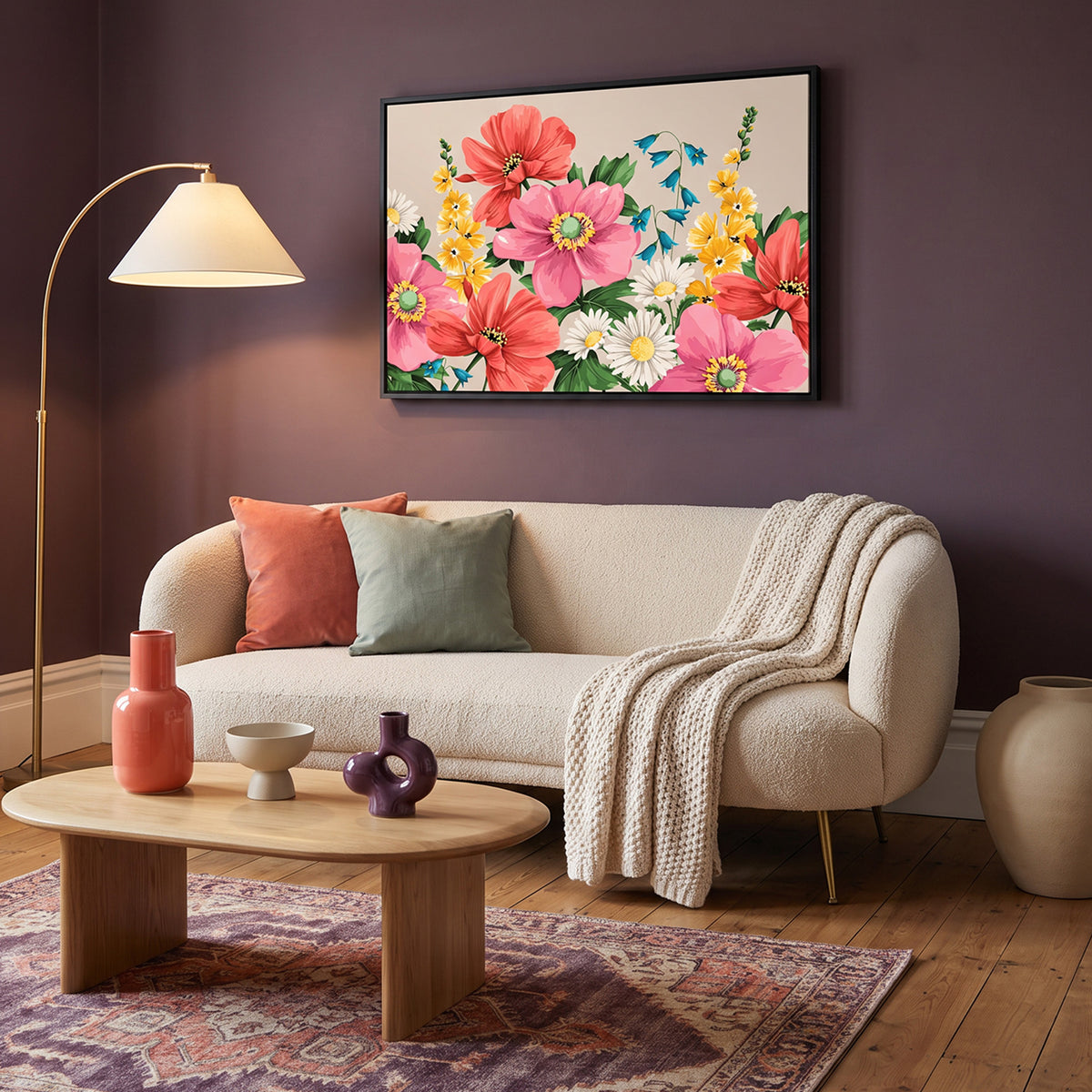 A Meadow Oatmeal framed floral wall art print hangs in a living room above a cream boucle sofa in a styled living room. The artwork features large pink and red flowers, white daisies, yellow blossoms, and blue leaves on a light background.